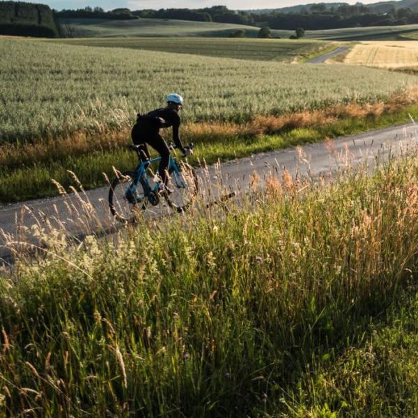 Eine Person fährt mit dem Rennrad auf der Landstraße entlang offener Felder in Vejle