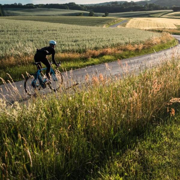 Eine Person fährt mit dem Rennrad auf der Landstraße entlang offener Felder in Vejle
