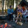 Eltern und Kinder genießen das Feuer an einem Schutzplatz und kochen über dem Feuer