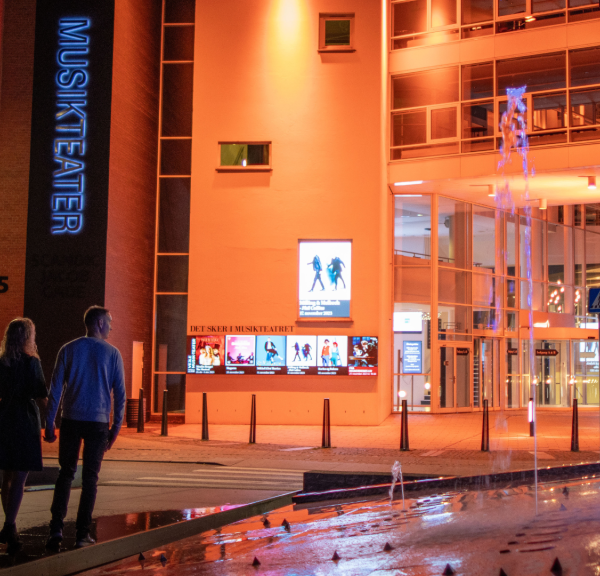 Ein Paar geht auf dem Weg zum Vejle Musikteater über den Kreisverkehr mit dem Brunnen vor dem Musiktheater