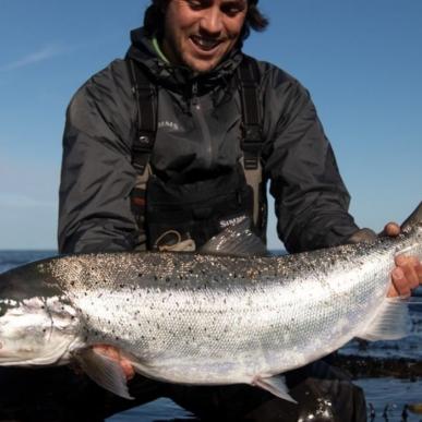 Ein Fischer mit einer Meerforelle in der Hand am Ufer