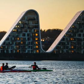 Menschen in Kajaks auf dem Vejle-Fjord mit Bølgen (der Welle) im Hintergrund
