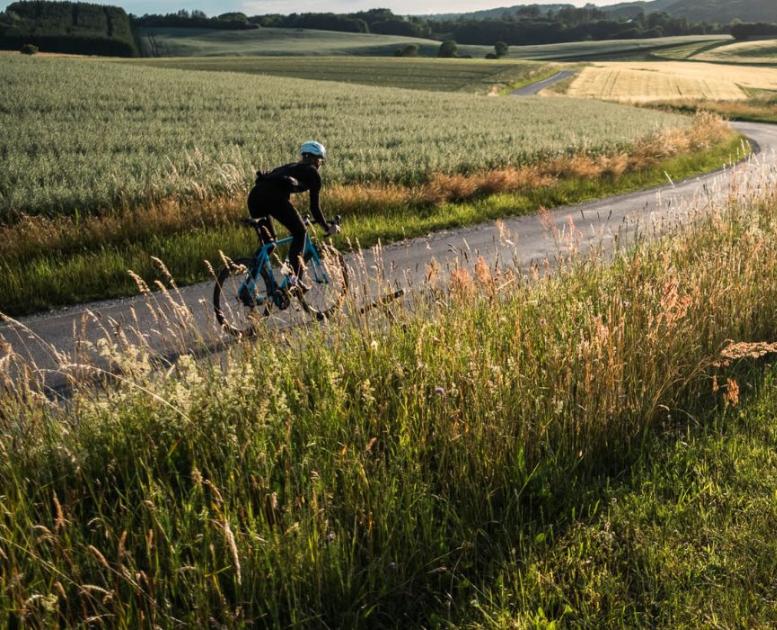 Eine Person fährt mit dem Rennrad auf der Landstraße entlang offener Felder in Vejle