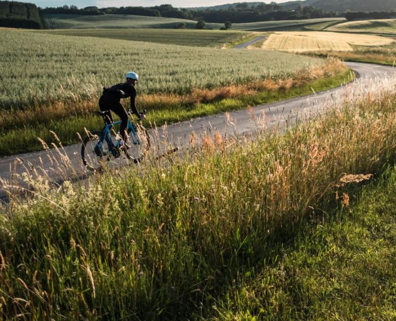 Eine Person fährt mit dem Rennrad auf der Landstraße entlang offener Felder in Vejle