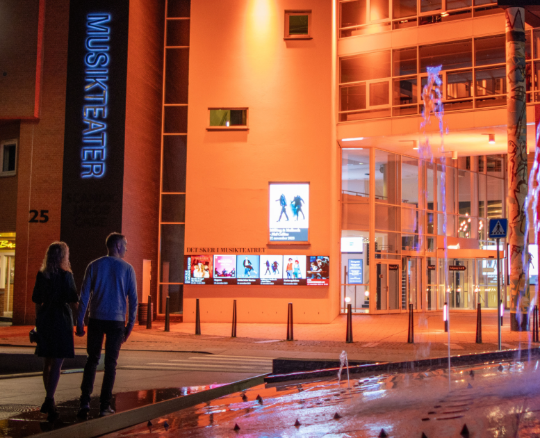 Ein Paar geht auf dem Weg zum Vejle Musikteater über den Kreisverkehr mit dem Brunnen vor dem Musiktheater