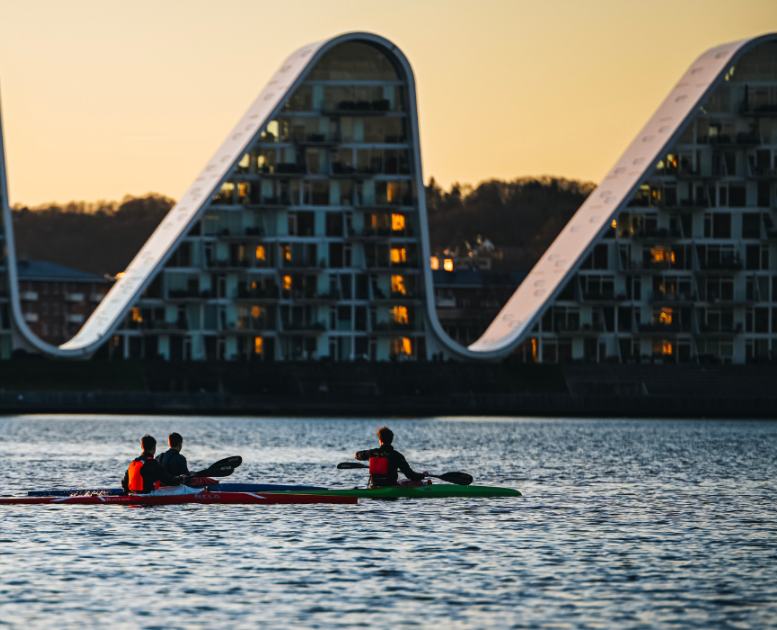 Menschen in Kajaks auf dem Vejle-Fjord mit Bølgen (der Welle) im Hintergrund