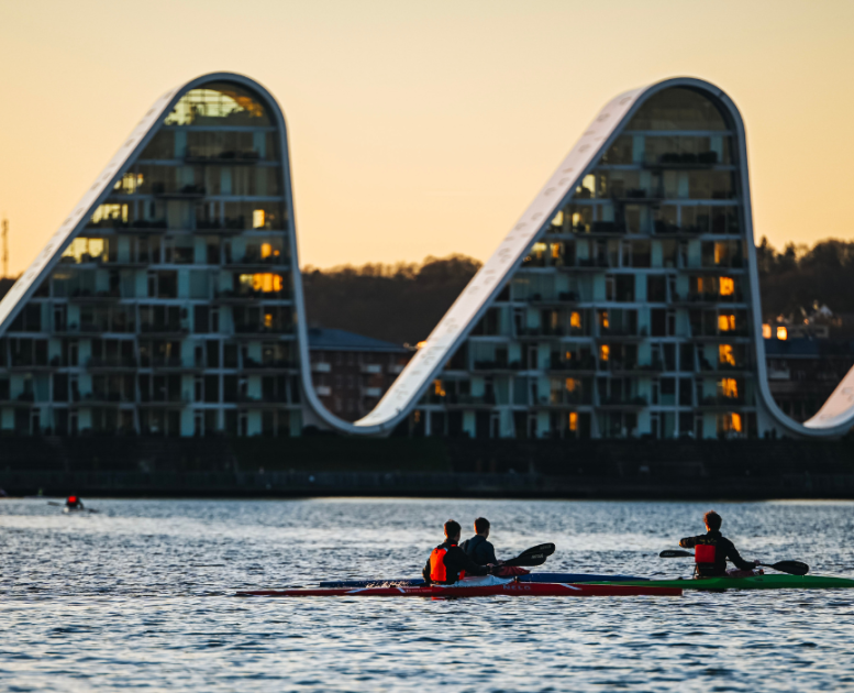 Menschen in Kajaks auf dem Vejle-Fjord mit Bølgen (der Welle) im Hintergrund