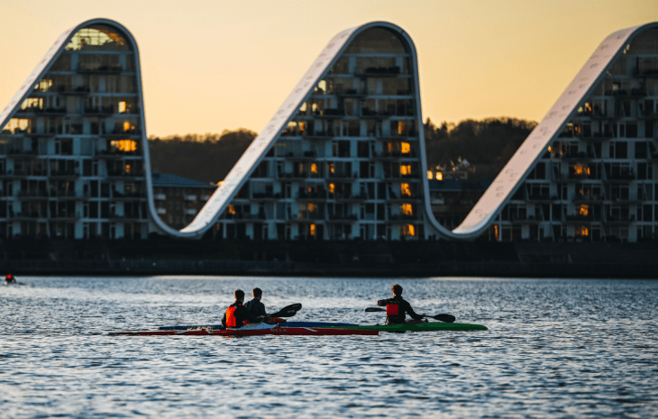 Menschen in Kajaks auf dem Vejle-Fjord mit Bølgen (der Welle) im Hintergrund